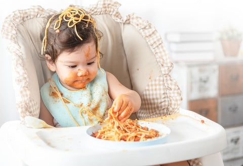 Baby in highchair which food over head and face